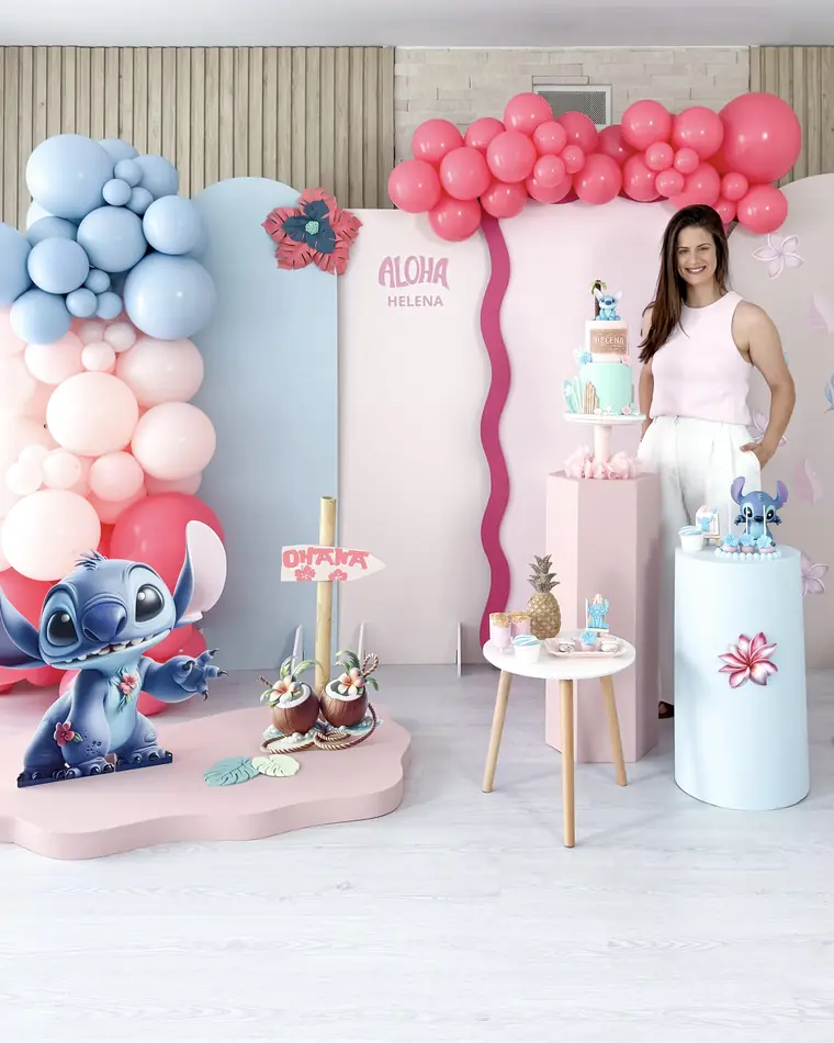 Cenário de festa em tons de rosa e azul com painéis ondulados, balões e figuras decorativas.