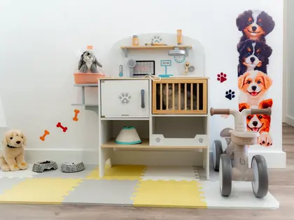 Zona de jogo do Mini & Magic com peluches, tapete e triciclo.