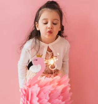 Menina vestida de rosa a soprar uma vela de aniversário.