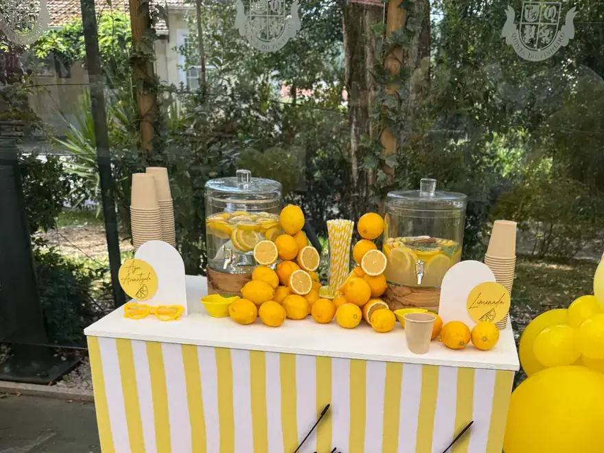 Bar de limonada amarelo e branco decorado para uma festa ao ar livre.